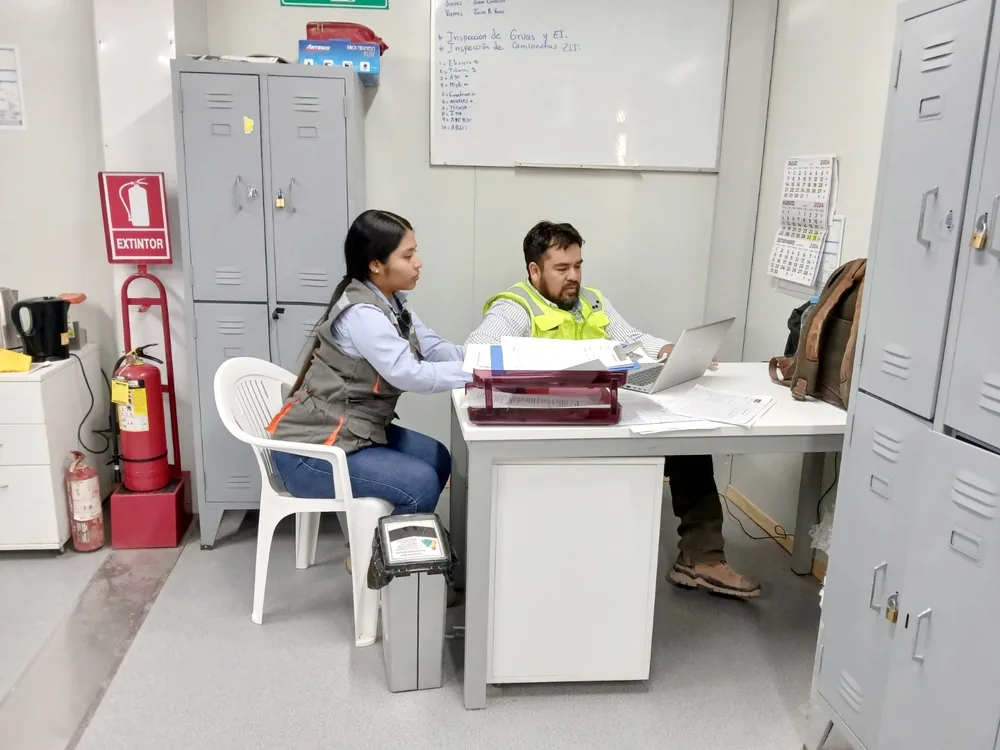 Dos personas revisando archivadores y documentos en una oficina de obra con casilleros.