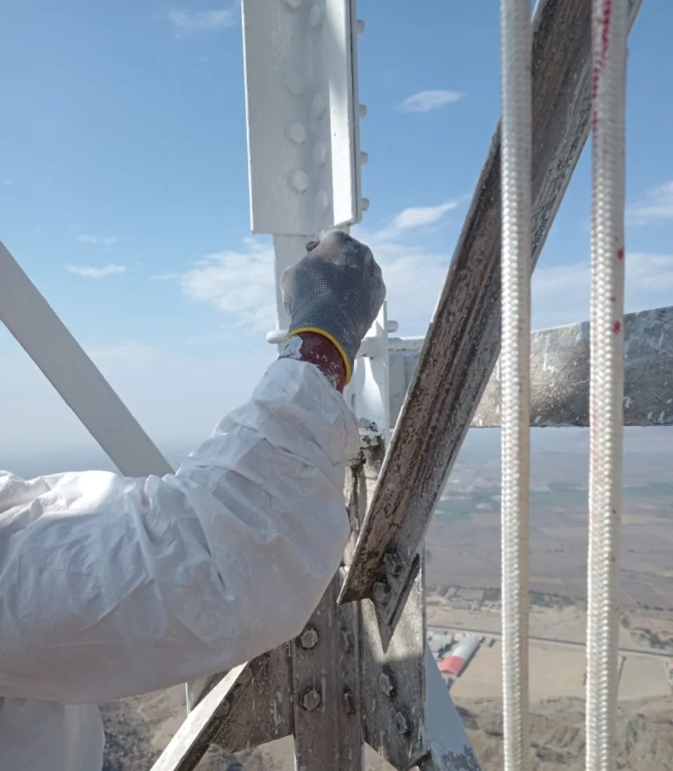 Operario con traje de protección blanco pintando un montante de la torre.