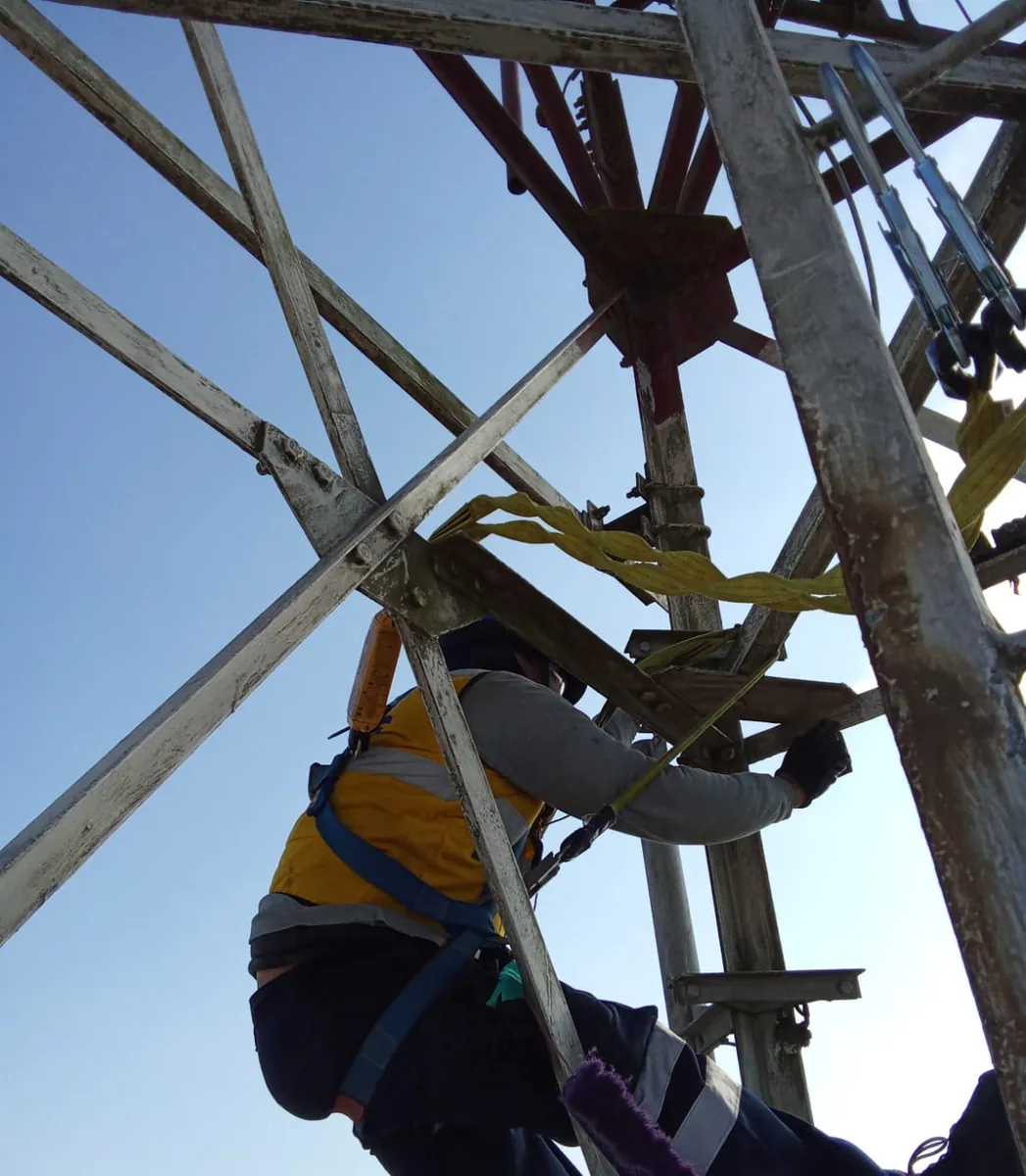 Técnico con arnés subiendo por la estructura de una torre, visto desde abajo.