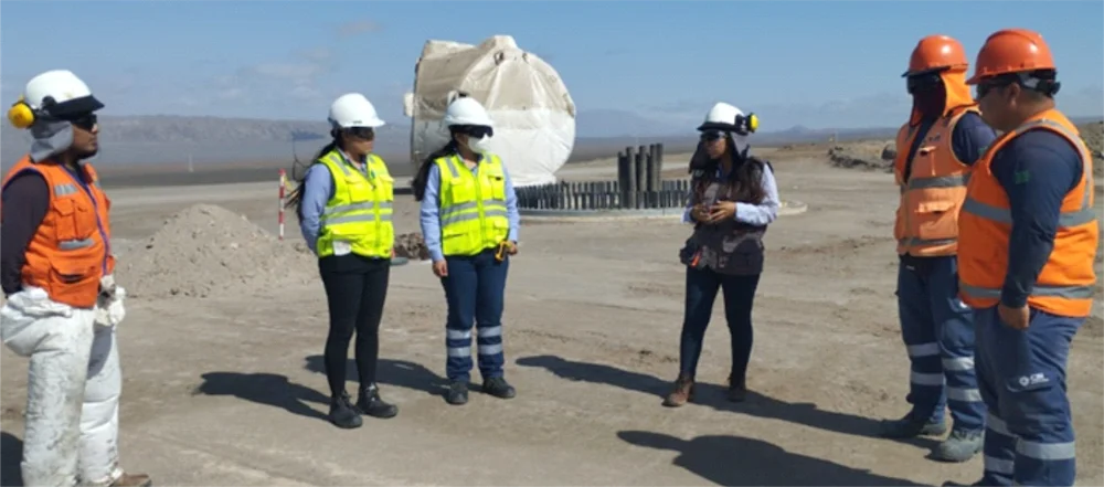 Charla de seguridad al aire libre con trabajadores y supervisoras usando equipo de protección personal.