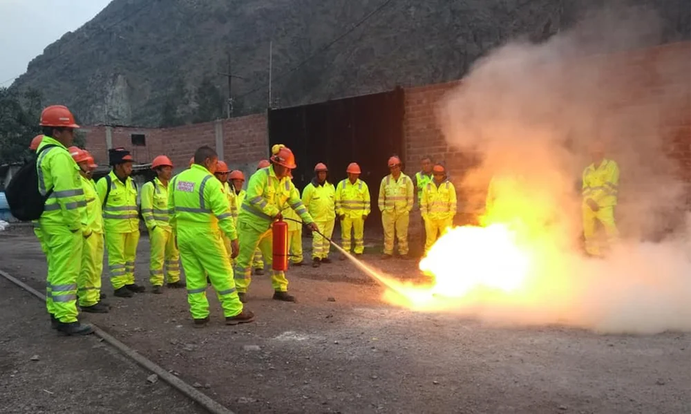 Práctica de extinción de incendios: un trabajador usa un extintor sobre fuego controlado mientras el grupo observa.
